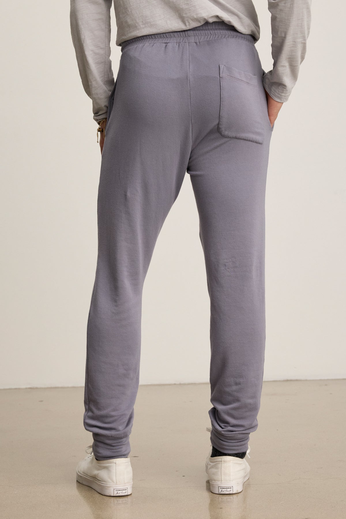A person in light gray Velvet by Graham & Spencer CROSBY JOGGER fleece pants and white sneakers, shown from the back, stands on a smooth floor against a plain background.