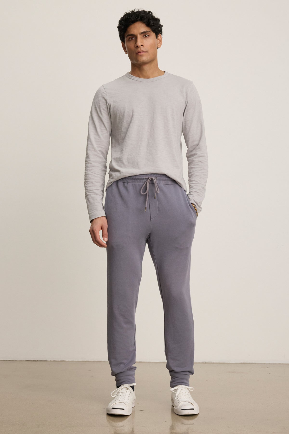A man stands against a plain background wearing a light gray long-sleeve shirt, Velvet by Graham & Spencer CROSBY JOGGER in gray, and white sneakers.