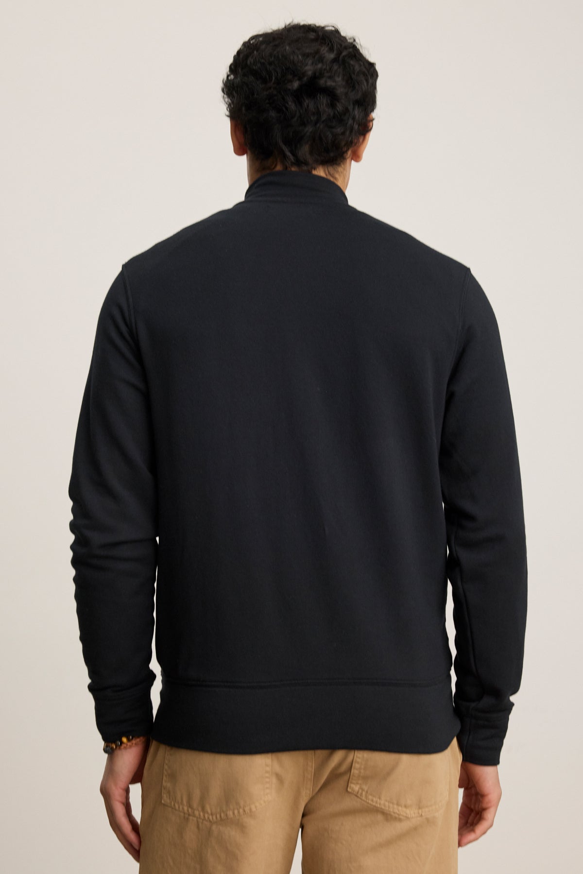 A person is shown from the back against a plain light background wearing the Velvet by Graham & Spencer DEMITRI FULL ZIP black mock neck jacket with tan pants.