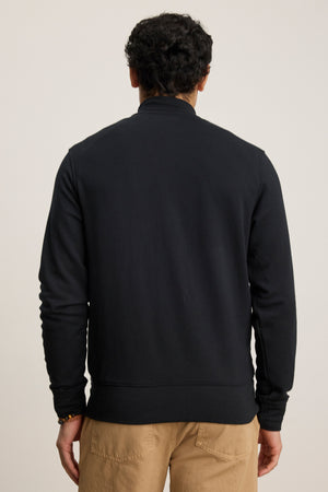 A person is shown from the back against a plain light background wearing the Velvet by Graham & Spencer DEMITRI FULL ZIP black mock neck jacket with tan pants.