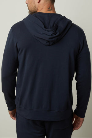 A man wearing a navy blue RODAN HOODIE with the hood down, made from luxe fleece by Velvet by Graham & Spencer, stands with his back to the camera.