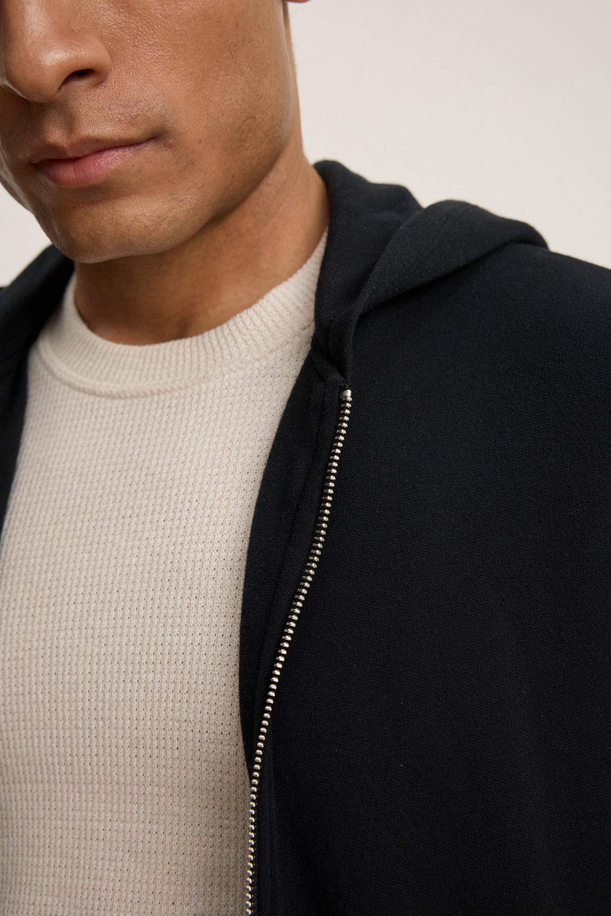 A close-up shows a person from the shoulders up, partially revealing their face, wearing a light beige textured shirt layered under the RODAN HOODIE by Velvet by Graham & Spencer.