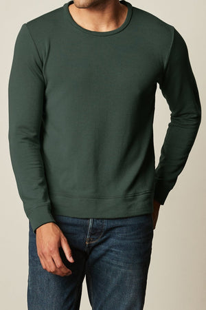 A man wearing the Velvet by Graham & Spencer SOREN LUXE FLEECE PULLOVER and stretch jeans.