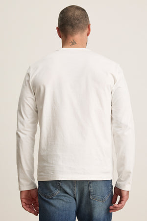 A person shown from the back wears the Velvet by Graham & Spencer ANTONIO TEE—a relaxed fit, plain white cotton jersey long sleeve—paired with blue jeans, displaying a small arrow tattoo on their neck.