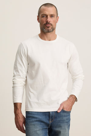 A man with short hair and a beard wears the ANTONIO TEE by Velvet by Graham & Spencer and blue jeans, standing against a neutral background.