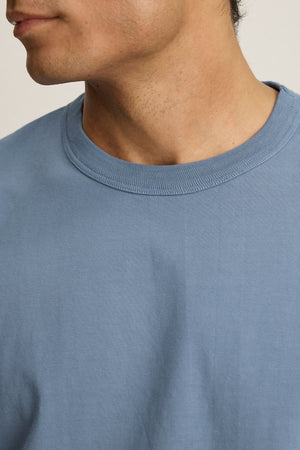 Close-up of a person wearing the WELLS TEE by Velvet by Graham & Spencer, a light blue cotton jersey crewneck, with the lower half of the face and neck visible.