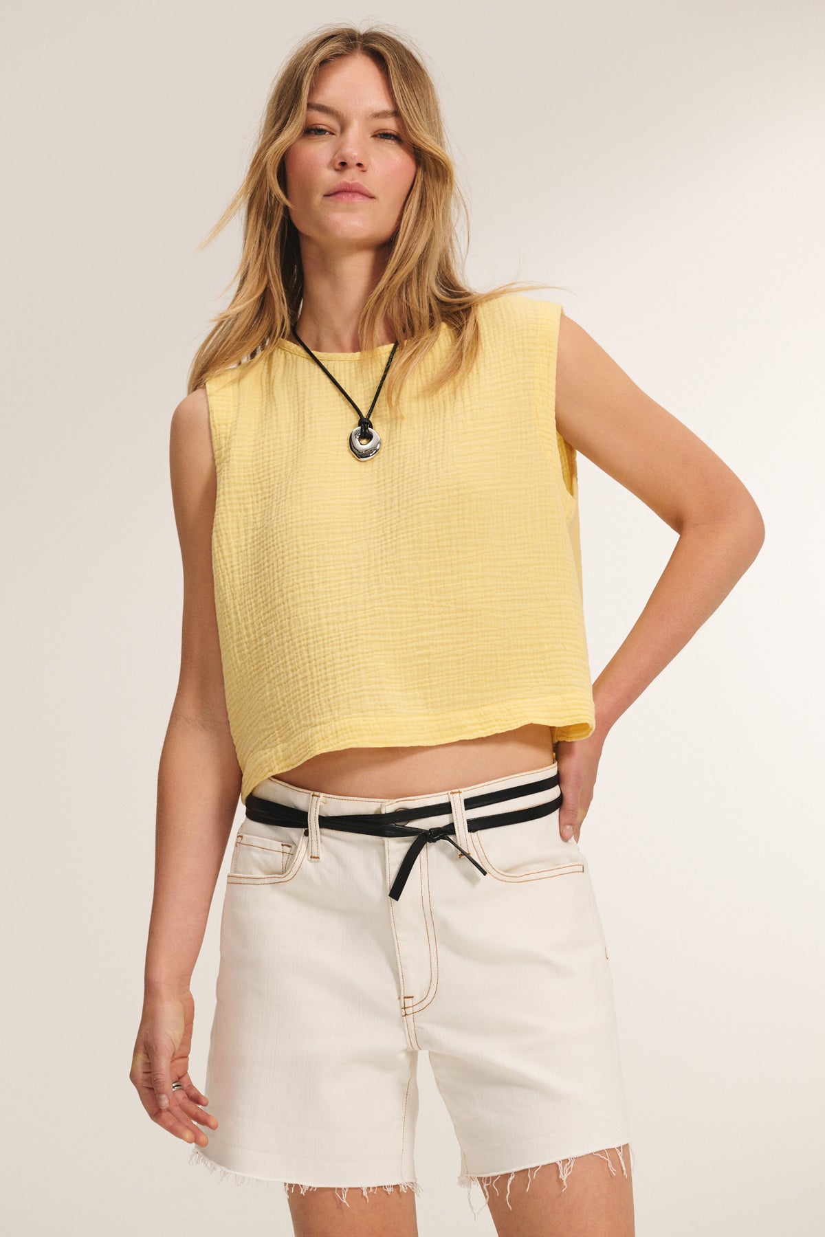 A woman wears the MILNEY COTTON GAUZE TOP by Velvet by Graham & Spencer, styled with white denim shorts and a black and white belt, standing against a plain background.-39161095585985