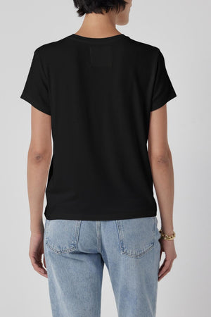 A person with short dark hair, wearing a tailored finish black SOLANA TEE by Velvet by Jenny Graham and light blue jeans, is standing with their back to the camera against a plain background.