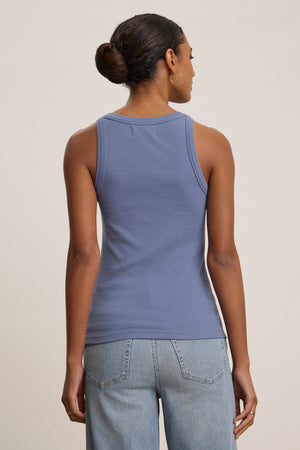 A person stands facing away in the CRUZ TANK TOP by Velvet by Jenny Graham and light blue jeans against a plain background—an effortless pick for any capsule wardrobe.