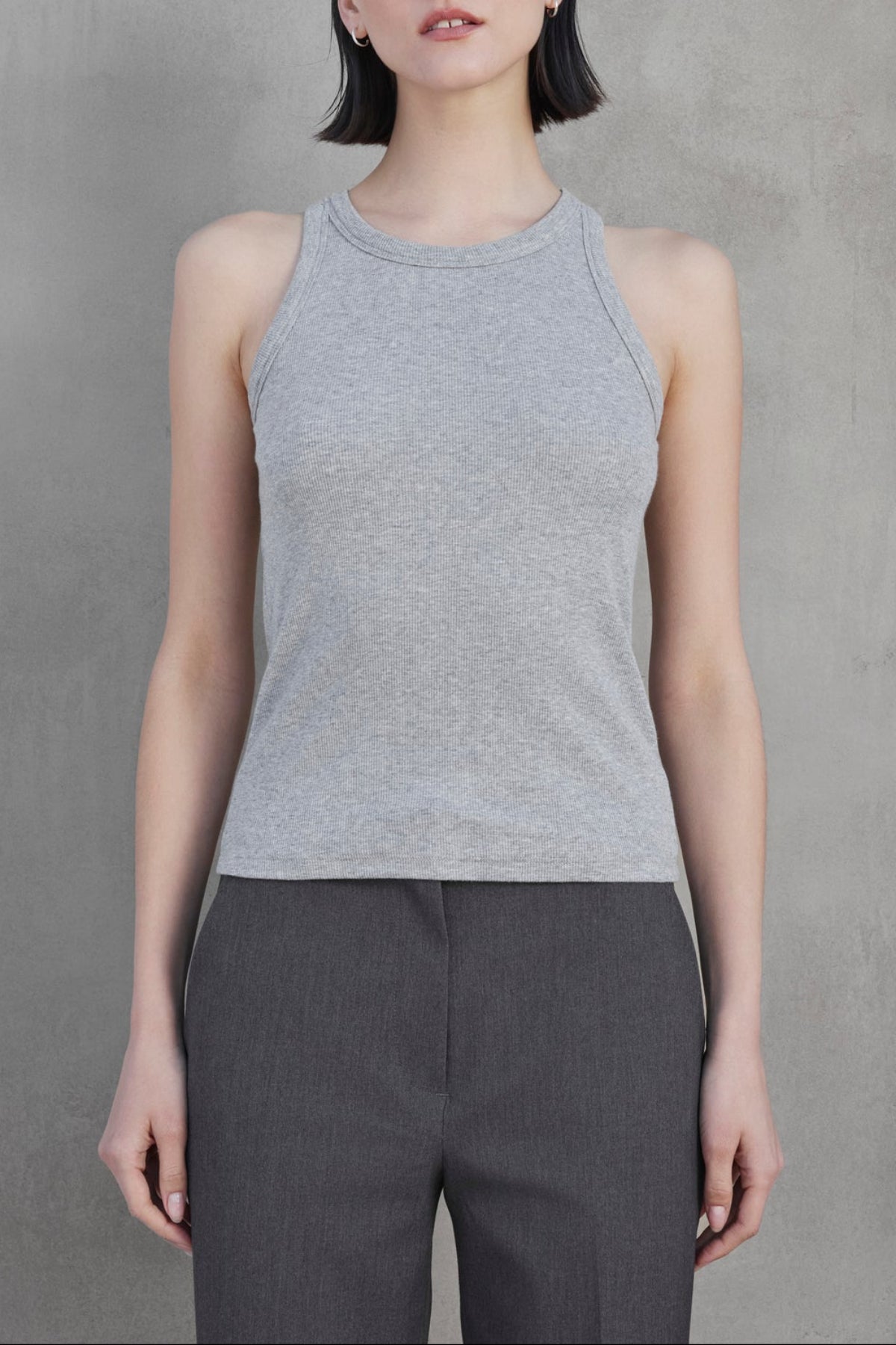 A person with short dark hair wears the versatile CRUZ TANK TOP from Velvet by Jenny Graham in a gray sleeveless top and dark gray pants, standing against a plain gray background.-37659959066817