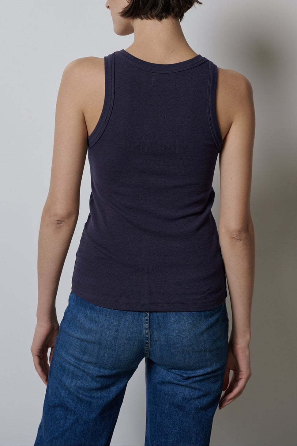 The woman's back view showcases a form-fitting CRUZ tank top by Velvet by Jenny Graham paired with jeans that offer stretch for comfort.-35547435008193