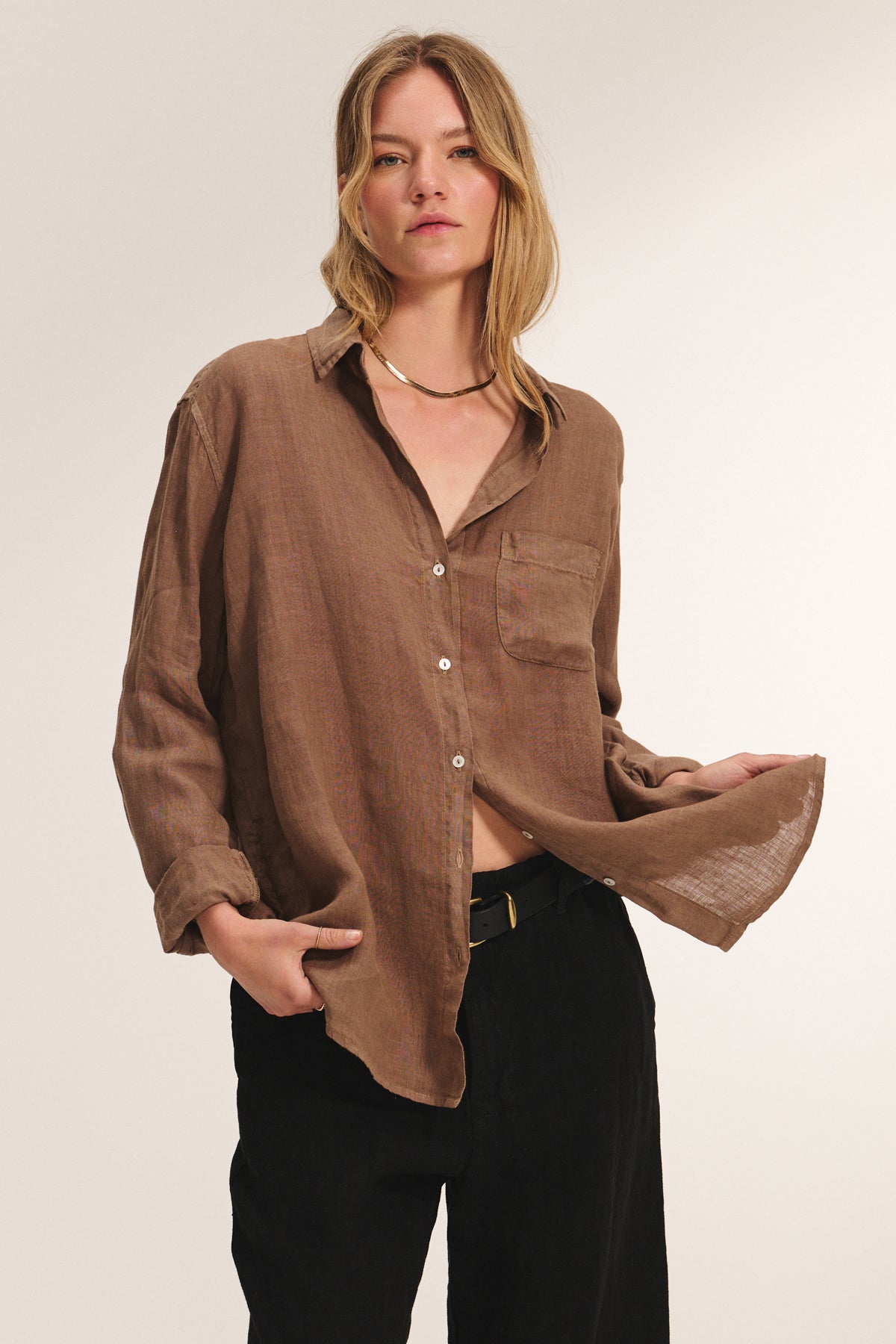 A woman models the MULHOLLAND LINEN SHIRT by Velvet by Jenny Graham, a relaxed, loose button-up with a scooped hemline, styled with black pants against a plain background.
