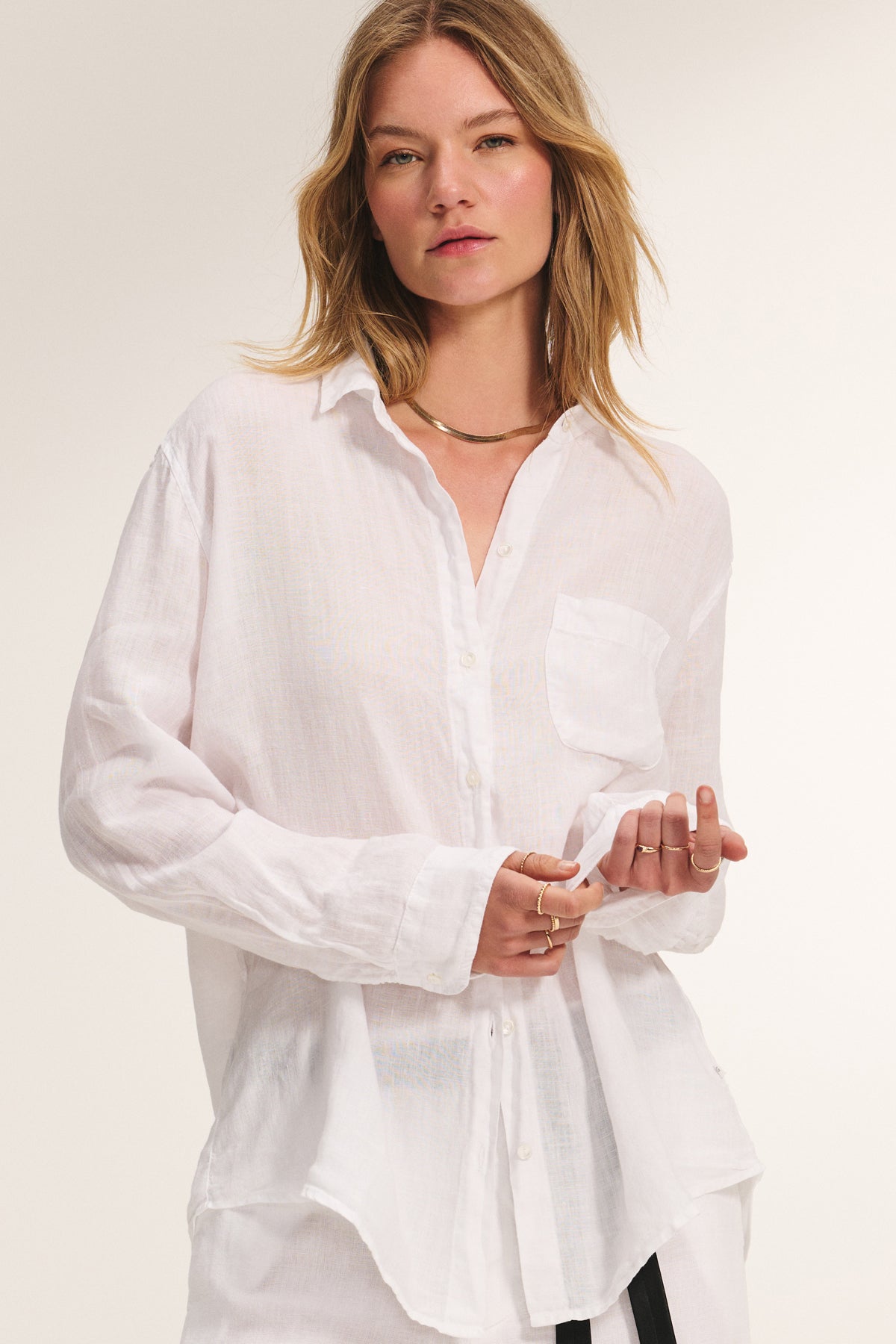 A woman in the MULHOLLAND LINEN SHIRT by Velvet by Jenny Graham—featuring a relaxed fit, chest pocket, and white linen fabric—wears light makeup and minimal jewelry while standing against a plain background.