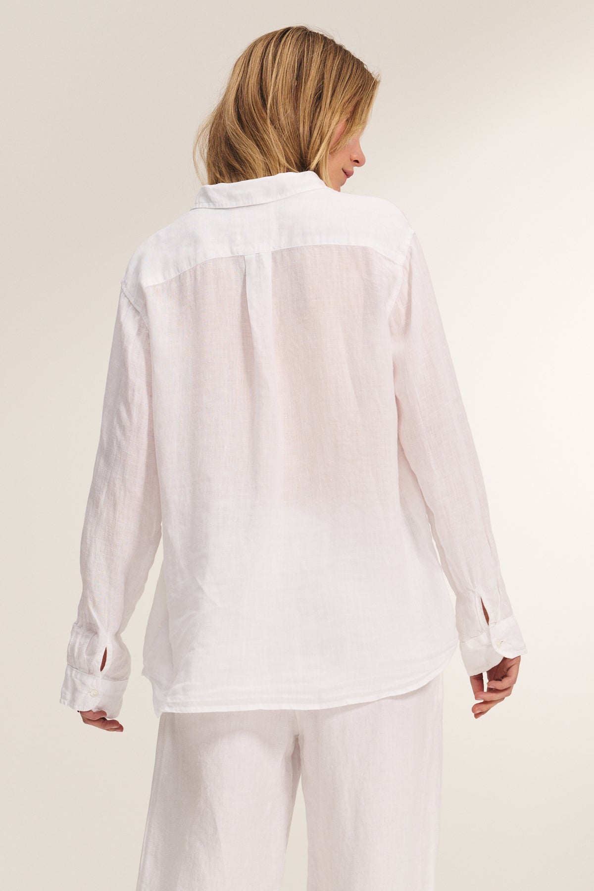 A woman faces away in the MULHOLLAND LINEN SHIRT by Velvet by Jenny Graham, styled with matching white pants against a neutral background.-39149231210689