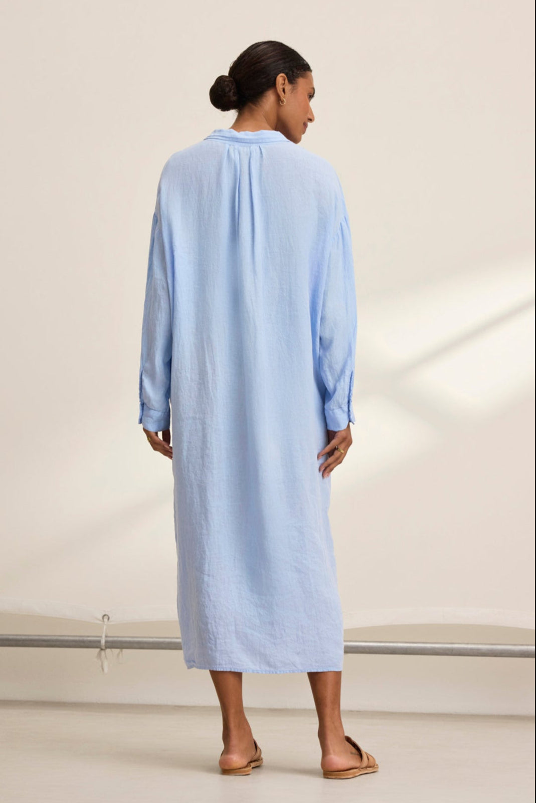 With their back to the camera, a person wears the breathable and versatile NICOLE LINEN DRESS in light blue, designed by Velvet by Graham & Spencer.