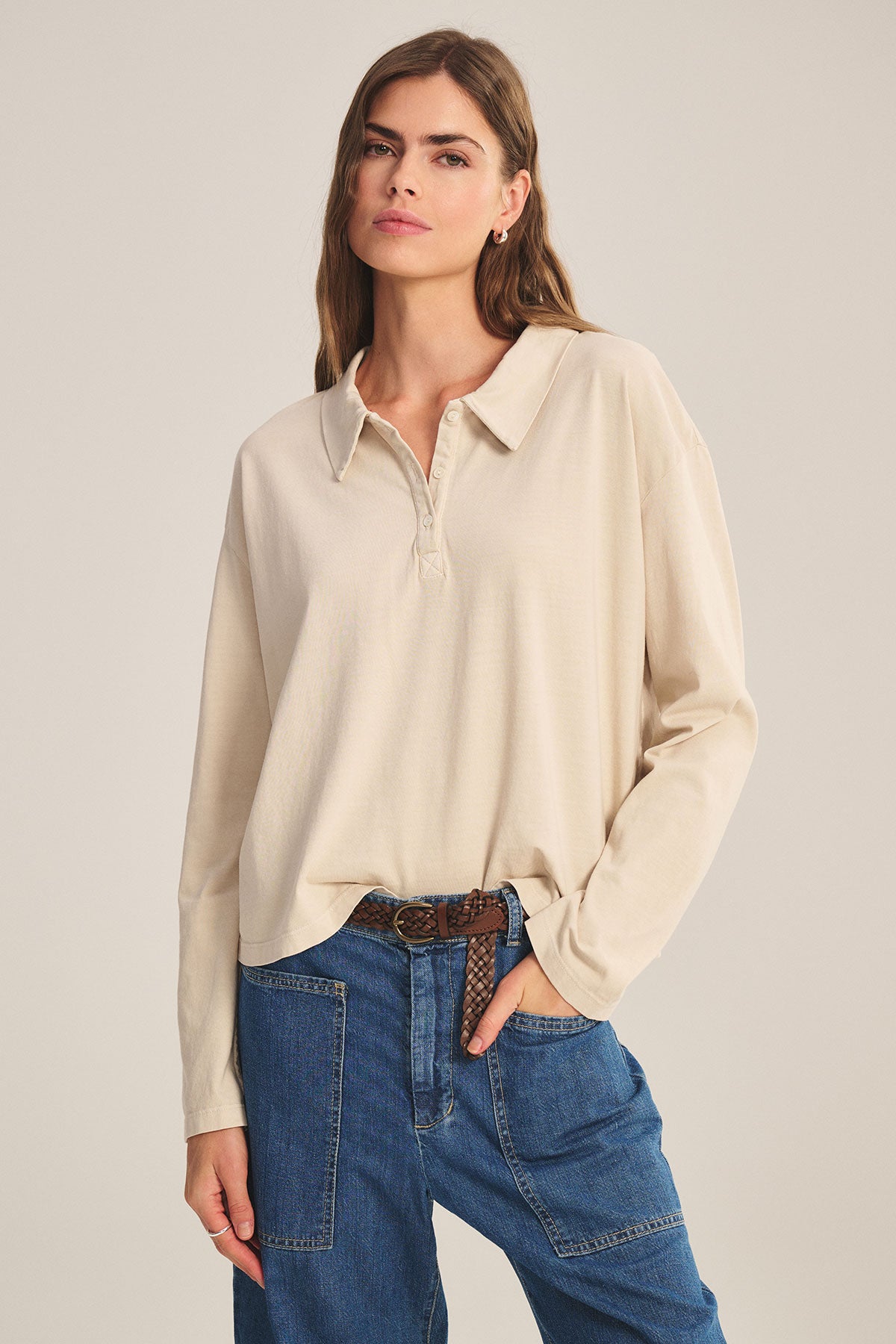 Woman wearing the NILLI POLO by Velvet by Graham & Spencer, a beige vintage cotton jersey collared shirt with a boxy fit, tucked into blue jeans, one hand in her pocket against a plain background.-39654977765569
