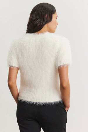 A woman with long dark hair is wearing the EILA FEATHER YARN SWEATER by Velvet by Graham & Spencer, along with black pants, facing away from the camera against a plain background.