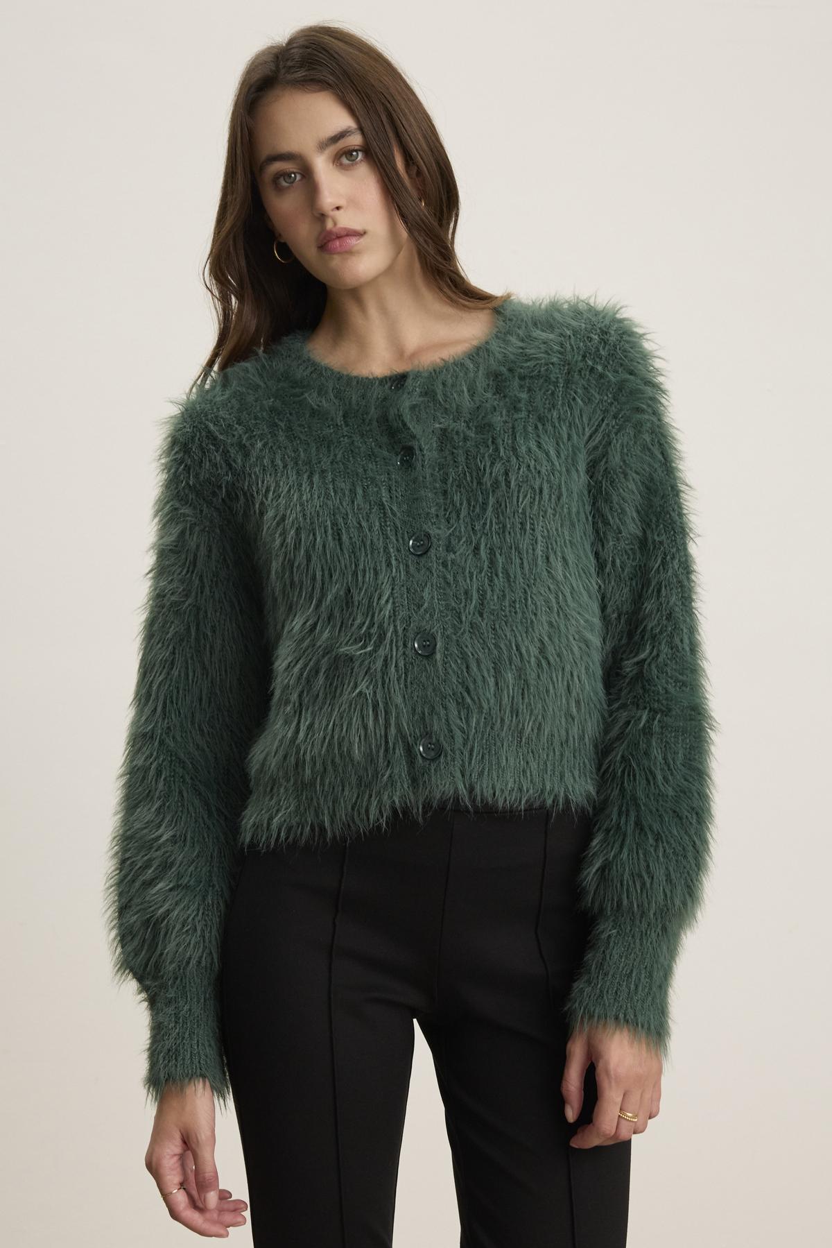 A person wearing a Holland Feather Yarn Cardigan by Velvet by Graham & Spencer and black pants stands against a plain backdrop, showcasing their versatile style.-38347945672897