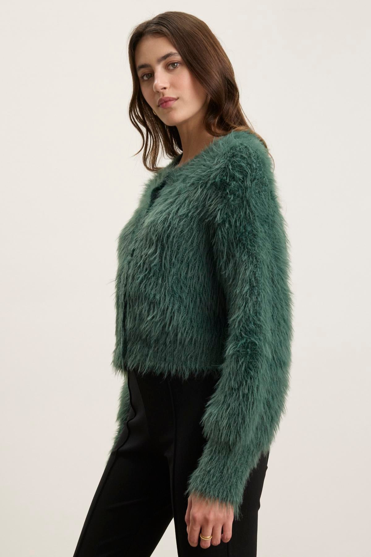 A person wearing the Velvet by Graham & Spencer HOLLAND FEATHER YARN CARDIGAN in a fuzzy green fabric, paired with black pants, stands against a plain background, showcasing their versatile style.-38347945574593