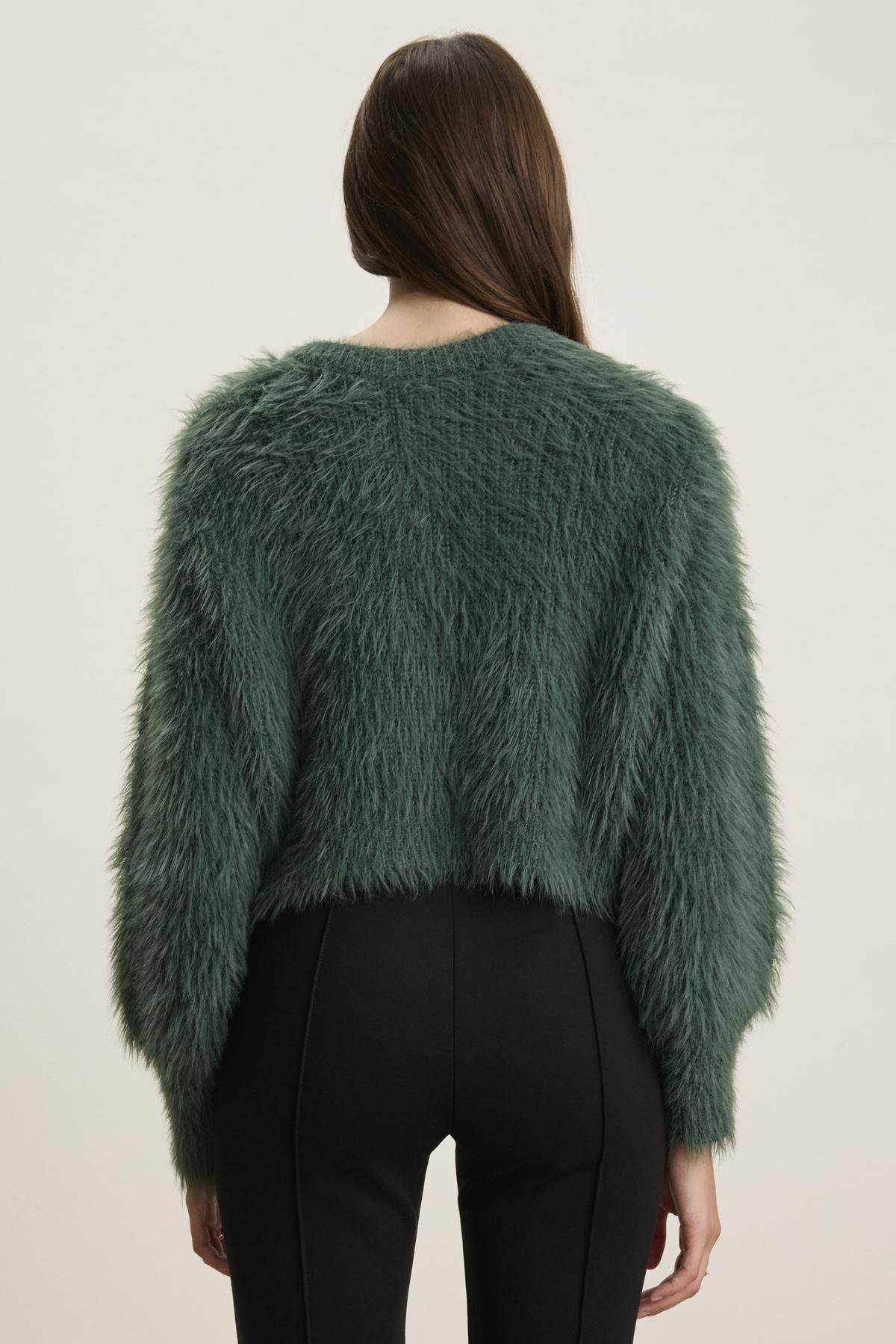 A person with long brown hair is wearing a green HOLLAND FEATHER YARN CARDIGAN by Velvet by Graham & Spencer and black pants, viewed from the back against a plain background.-38347945607361