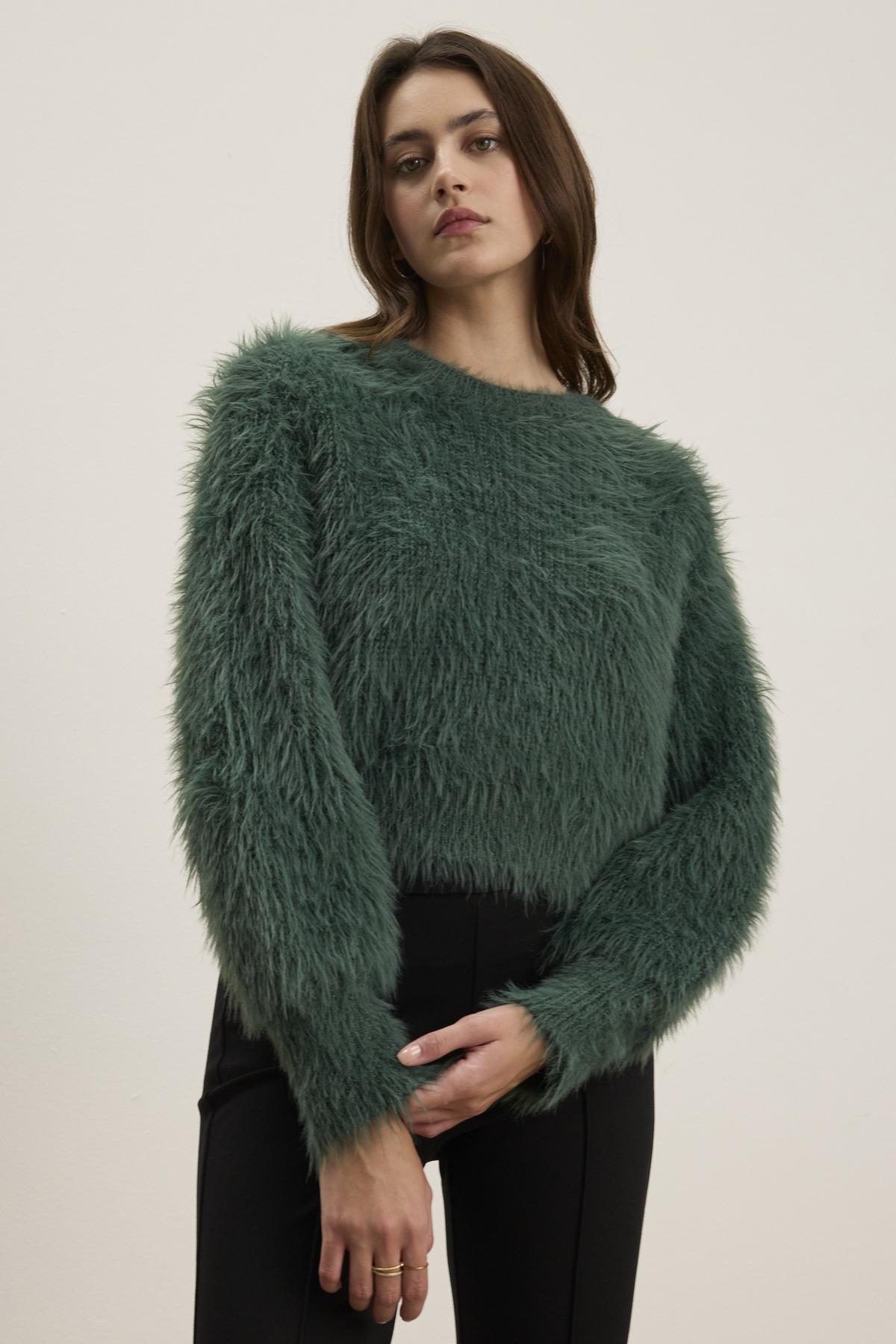 A person wearing the HOLLAND FEATHER YARN CARDIGAN by Velvet by Graham & Spencer and black pants stands against a plain background, showcasing their versatile style.