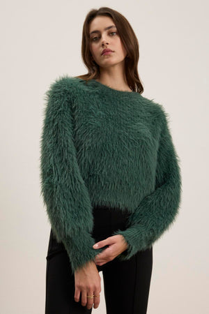 A person wearing the HOLLAND FEATHER YARN CARDIGAN by Velvet by Graham & Spencer and black pants stands against a plain background, showcasing their versatile style.