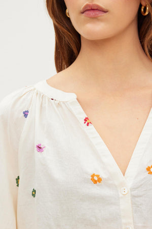 A woman wearing the Velvet by Graham & Spencer ARETHA EMBROIDERED BOHO TOP with embroidered flowers.