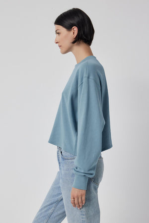 The model is wearing a blue MALIBU SWEATSHIRT crafted from organic cotton, paired with jeans by Velvet by Jenny Graham.