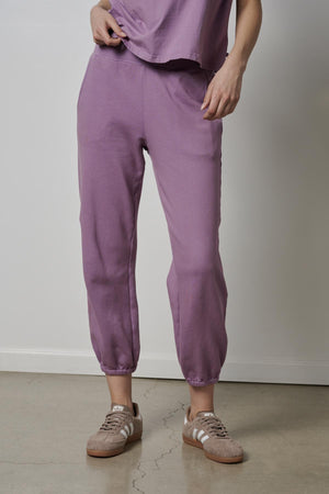A woman wearing purple ZUMA sweatpants and sneakers.