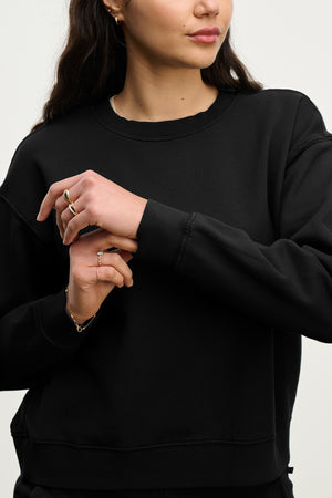 A woman adjusts her sleeve while wearing the Velvet by Jenny Graham YNEZ SWEATSHIRT. Only her upper body and hands are shown against a plain background.