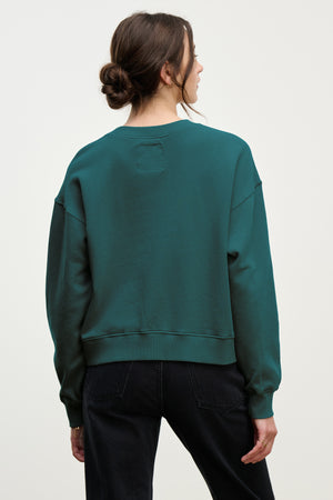 A person with brown hair in a low bun, wearing the Velvet by Jenny Graham YNEZ SWEATSHIRT and black jeans, is shown from the back against a plain light background.