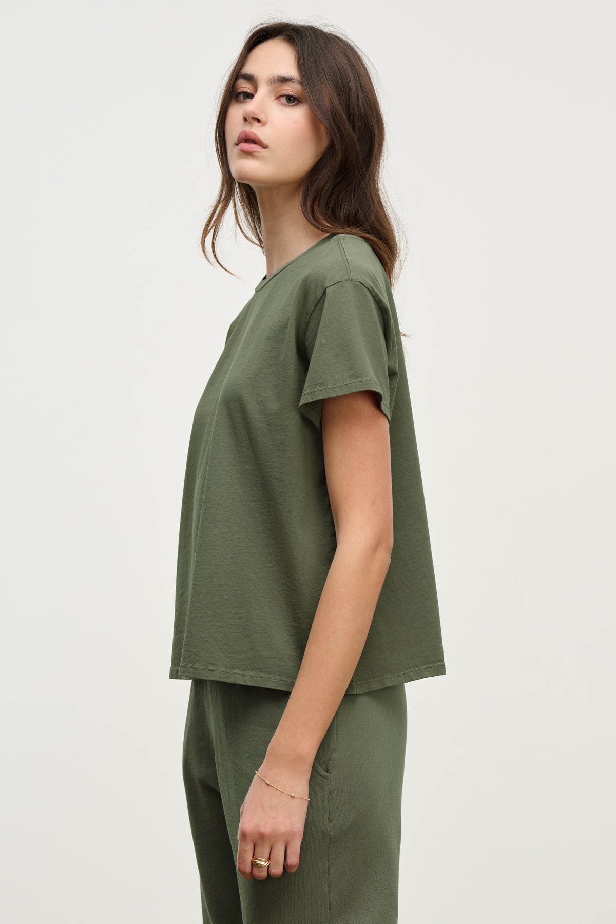 A person in a relaxed-fit green TOPANGA TEE and pants by Velvet by Jenny Graham, crafted from organic cotton, stands against a plain background, looking at the camera with a neutral expression.
