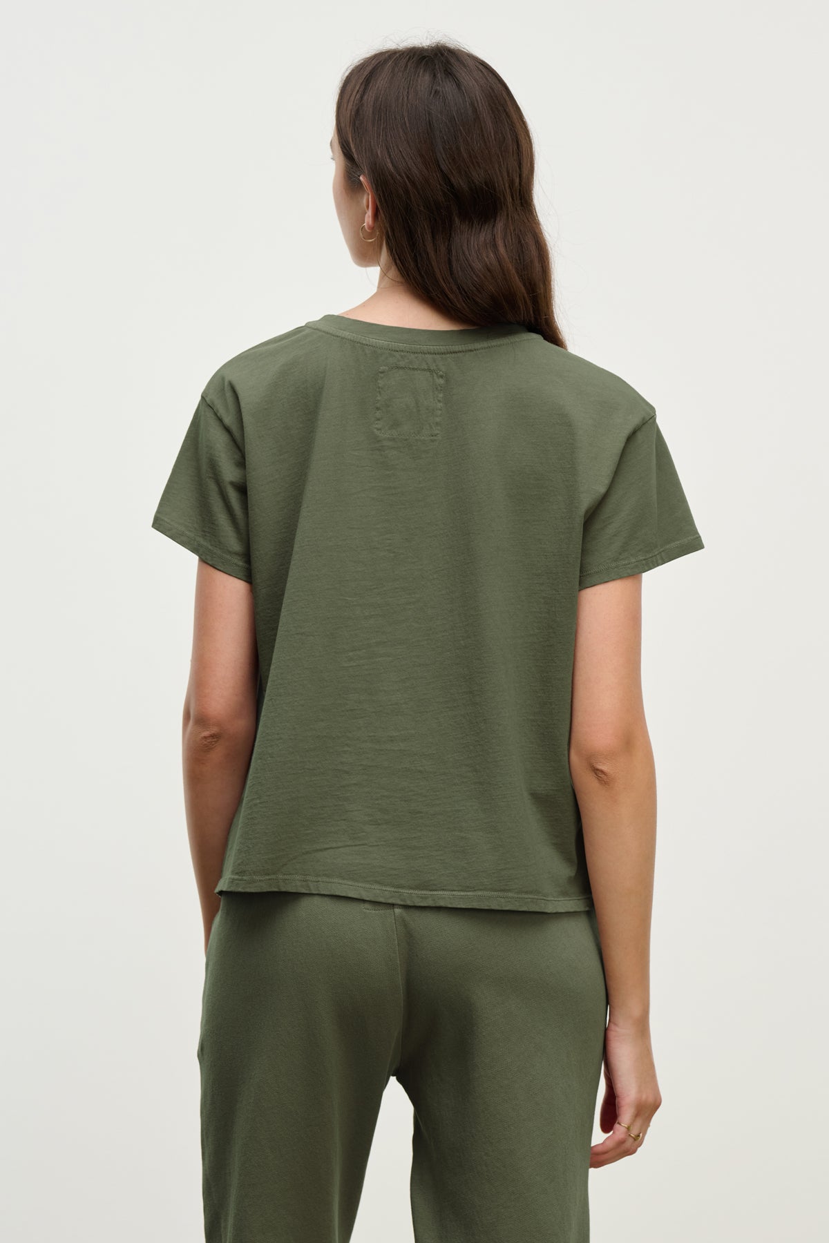 A person with long hair, wearing the relaxed-fit TOPANGA TEE by Velvet by Jenny Graham and organic cotton pants, stands facing away against a plain backdrop, capturing the essence of sustainable fashion.-38928282747073