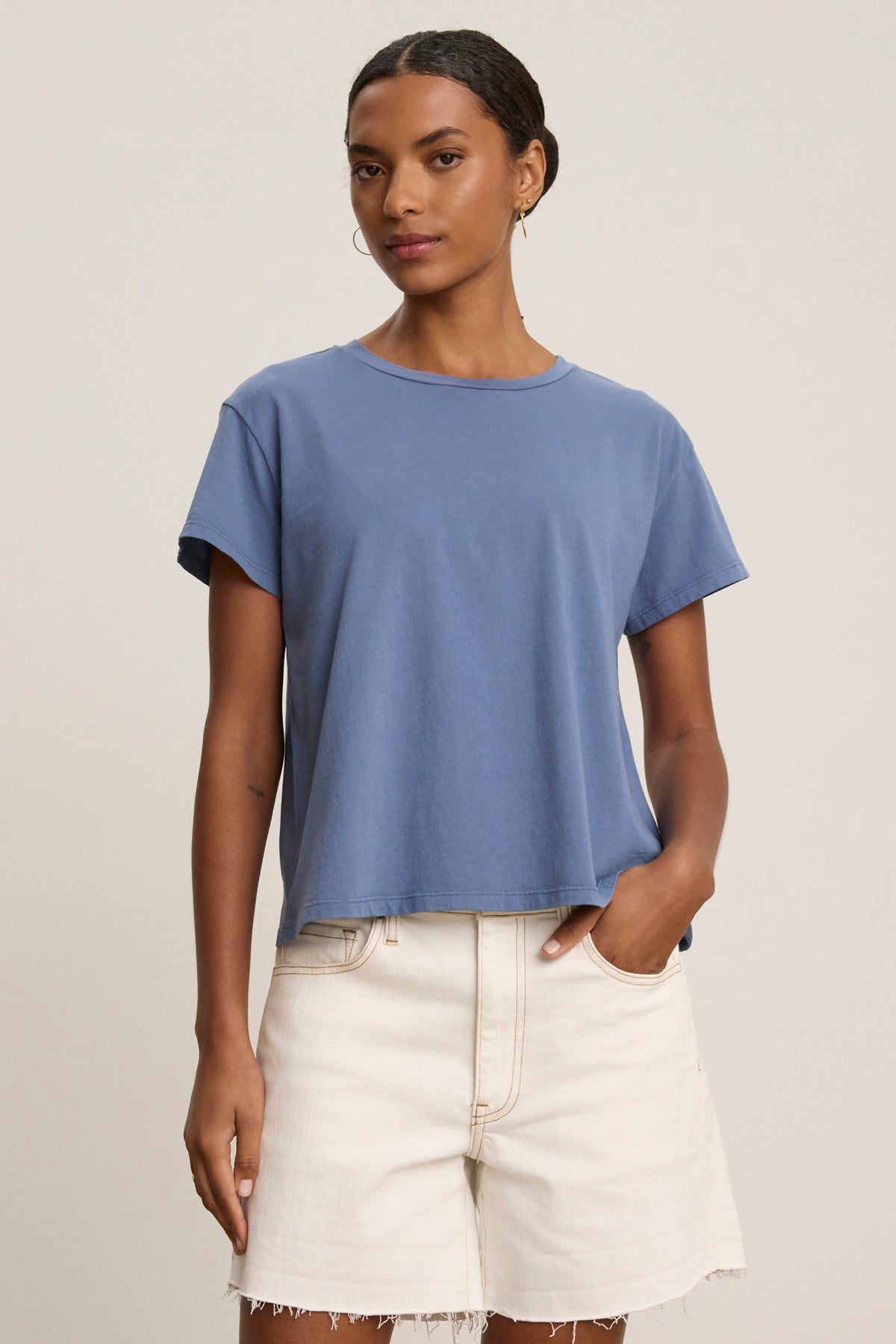 Wearing the Velvet by Jenny Graham TOPANGA TEE in a relaxed fit and light high-waisted shorts, a person stands against a plain background with one hand in their pocket.-39111849607361