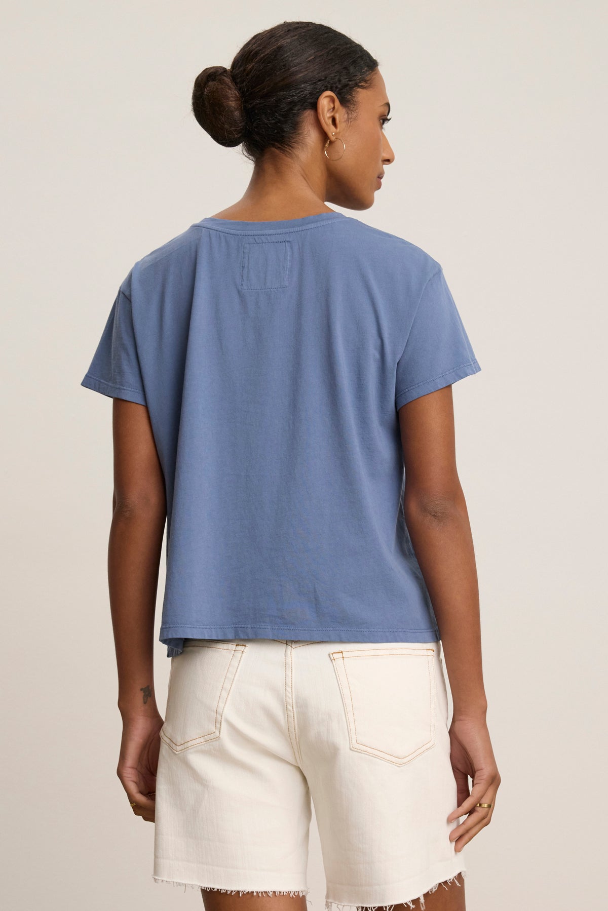 A person with hair in a bun, seen from behind against a neutral background, is wearing the TOPANGA TEE by Velvet by Jenny Graham in blue and white denim shorts.-39111850819777