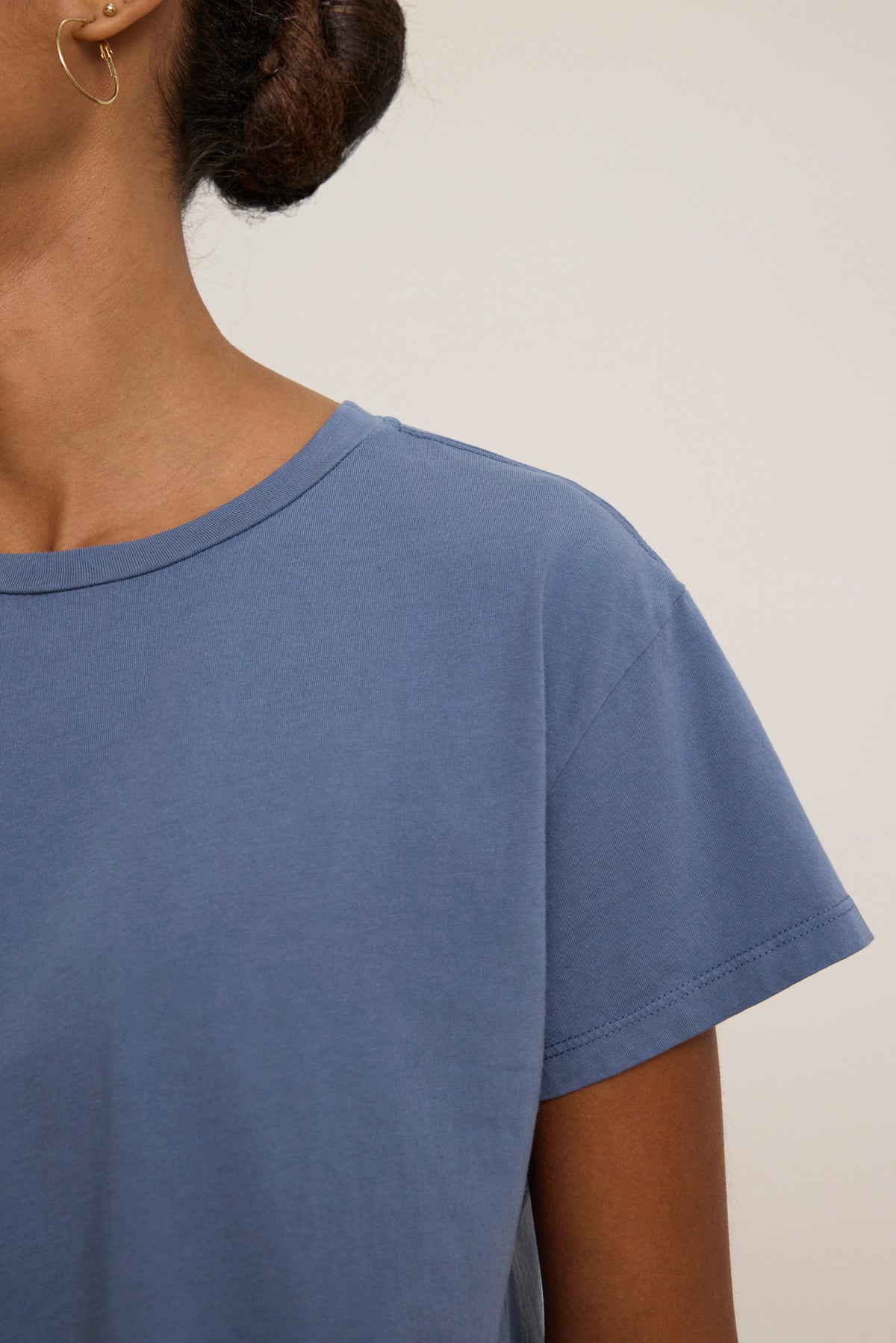 A close-up of a person wearing the Velvet by Jenny Graham TOPANGA TEE in blue with a gold hoop earring and their hair tied back. Their face is partially out of frame.-39111852196033