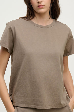 A woman wears the Velvet by Jenny Graham TOPANGA TEE in taupe—crafted from organic cotton with a relaxed fit—standing against a plain light background, ideal for easy transitions from work to workout.
