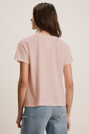 An individual in a Velvet by Jenny Graham TOPANGA TEE, light pink and made from organic cotton, with blue jeans, facing away.