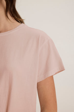 A partial view of someone in a relaxed-fit, light pink short-sleeved Velvet by Jenny Graham TOPANGA TEE, crafted from soft organic cotton, against a plain background.