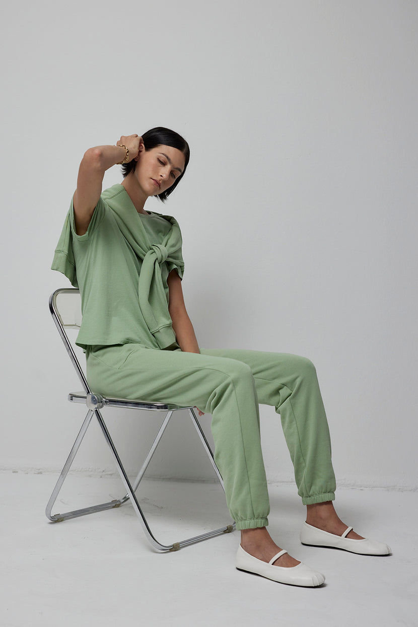 Sentence with replaced product: A woman is sitting on a chair in Velvet by Jenny Graham's WESTLAKE SWEATPANT in sage green.