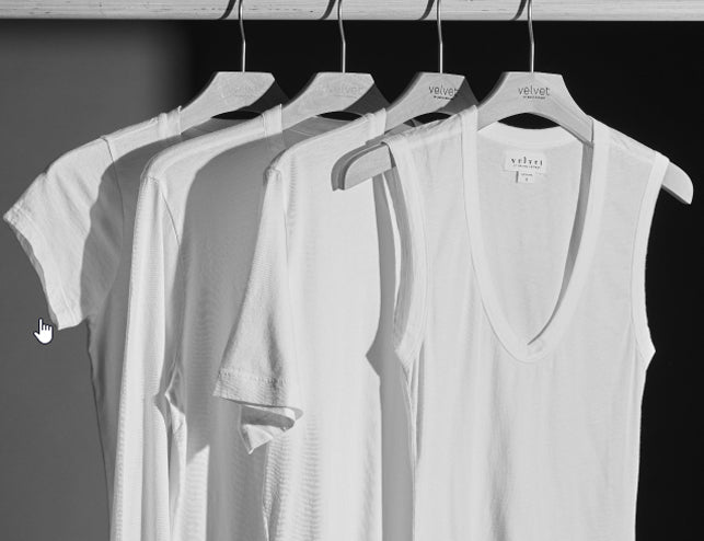 Four white shirts hanging on a rack in a grayscale image.