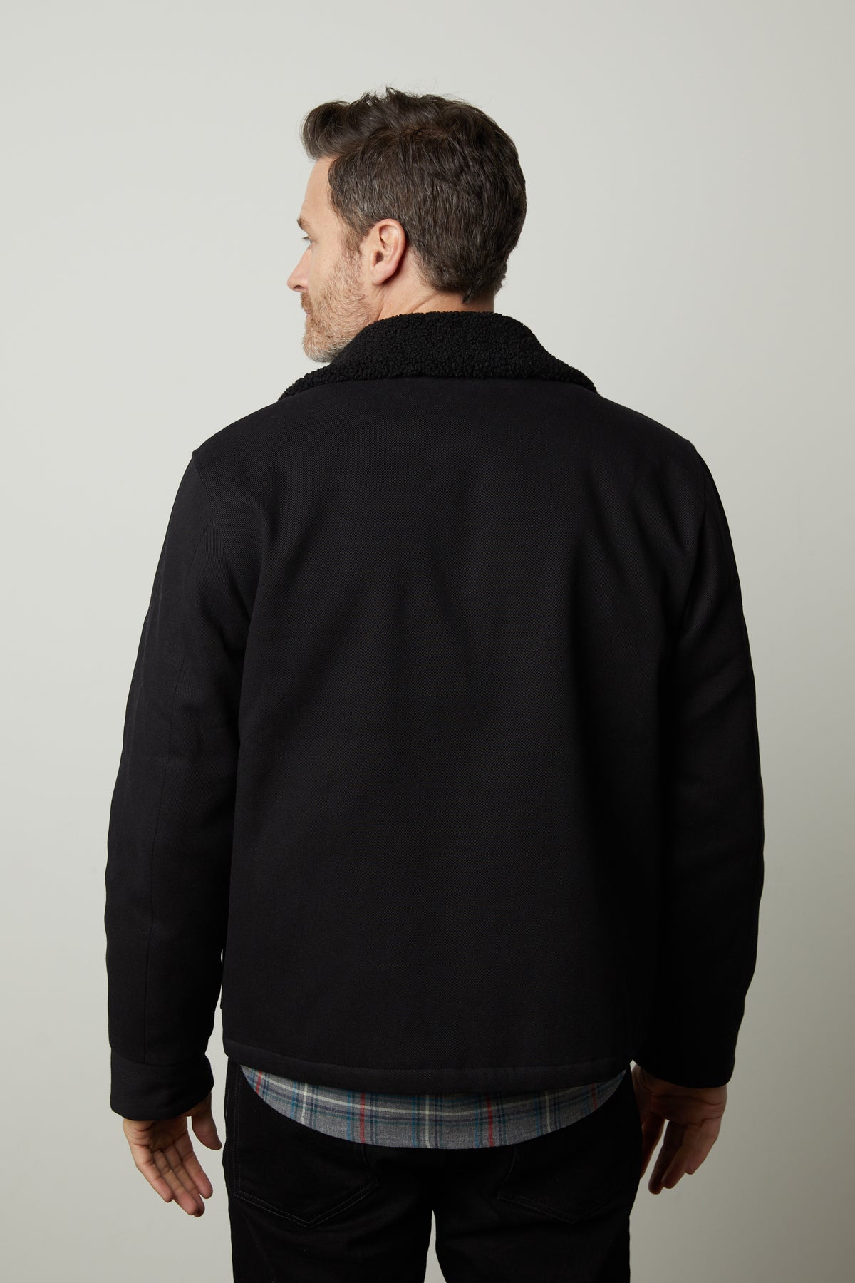 Man with short hair viewed from behind, wearing a Velvet by Graham & Spencer CASH JACKET with a zipper front and faux sherpa collar over a plaid shirt. The background is plain and light-colored.-35472047145153
