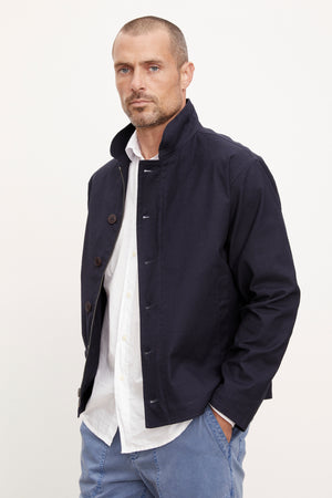 A man wearing a Velvet by Graham & Spencer Marlon Zip-Up Jacket with a front zipper and white pants.