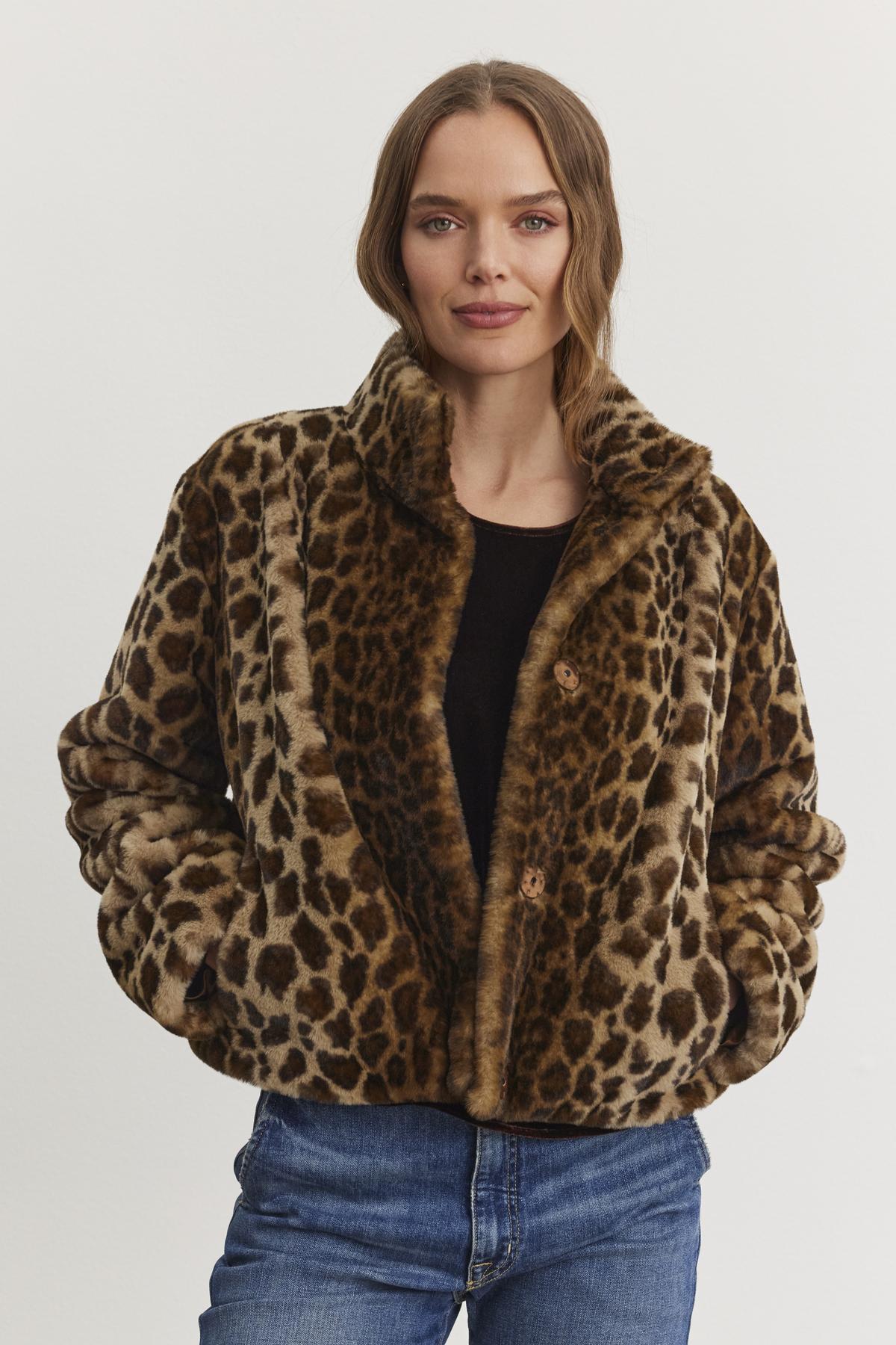 A woman wearing the VALLI FAUX FUR JACKET by Velvet by Graham & Spencer and blue jeans stands against a plain background.