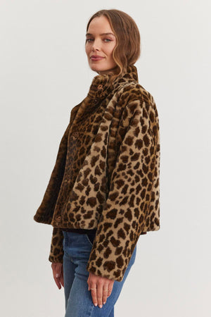 A woman in the VALLI FAUX FUR JACKET by Velvet by Graham & Spencer and blue jeans stands against a plain background.