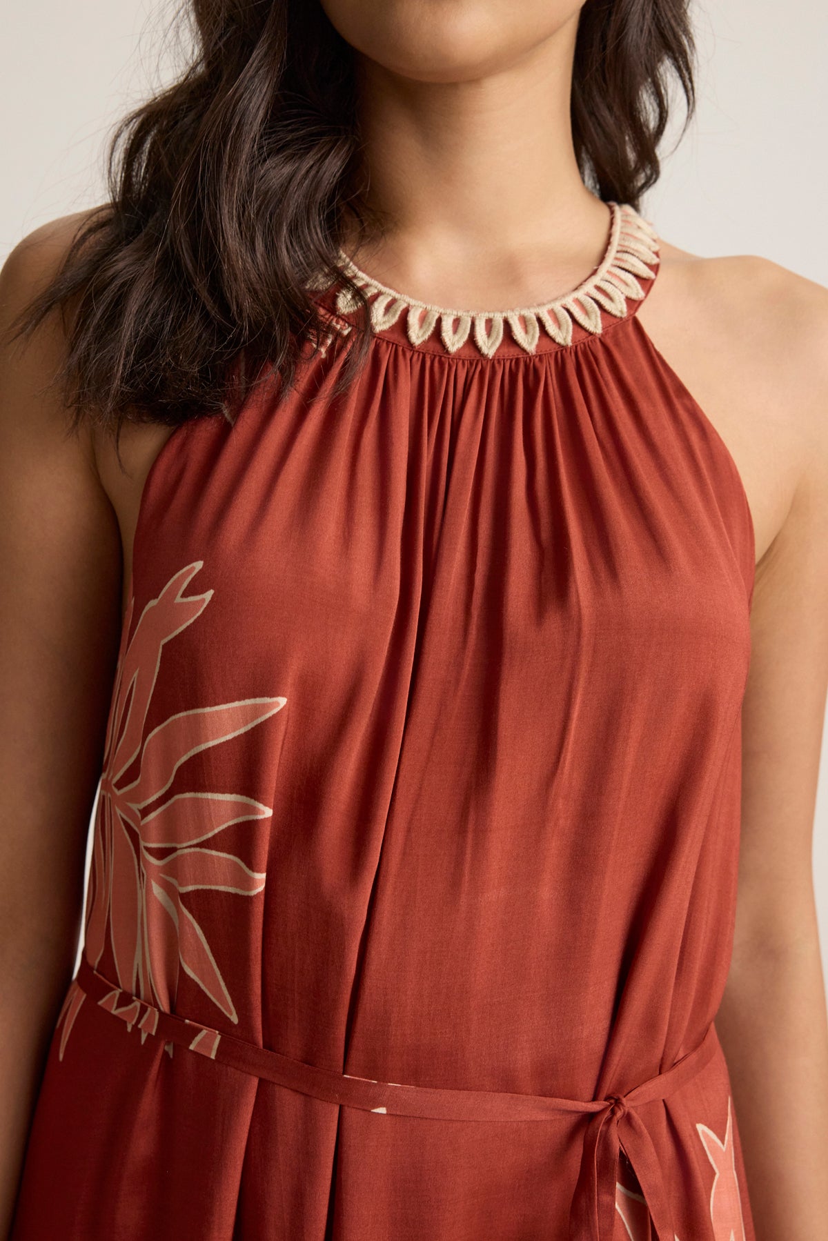 A woman wears the ODESSA DRESS by Velvet by Graham & Spencer—a sleeveless rust-colored maxi with a gathered neckline, cream trim, and a light floral print on one side.-39123393577153