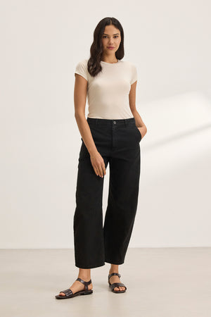 Someone in a light t-shirt and Velvet by Graham & Spencer's ALEXIS PANT, cropped at the ankle, stands against a plain background with hands in pockets.