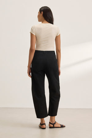 A person with long hair wearing a beige t-shirt and Velvet by Graham & Spencer's ALEXIS PANT, cropped at the ankle, stands against a plain white background, facing away from the camera.