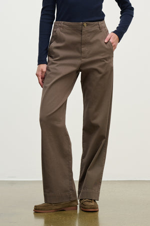 A person wears the DEN PANT by Velvet by Graham & Spencer—brown cotton twill wide-leg pants with an elastic waistband—paired with a navy long-sleeve shirt and brown shoes, standing against a plain light background.