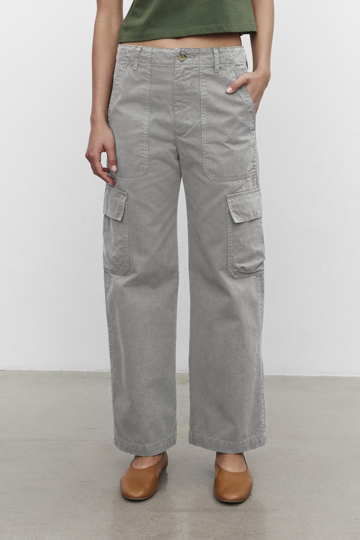A person wearing the stylish MAKAYLA PANT by Velvet by Graham & Spencer, featuring handy cargo pockets, pairs them with a green top and brown shoes while standing against a white background. This versatile wardrobe choice is both chic and practical for any occasion.-38372889198785